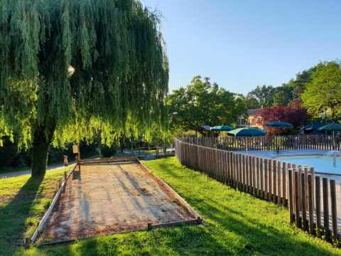 Giornata di sole a Huttopia Sarlat con campo da bocce, salice, piscina e ombrelloni verdi.