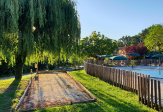 Sunny day at Huttopia Sarlat holiday park with bocce court, willow tree, pool and green umbrellas.