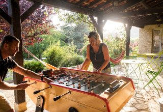 To personer spiller bordfodbold udendørs på en overdækket terrasse i Huttopia Sarlat, Frankrig.