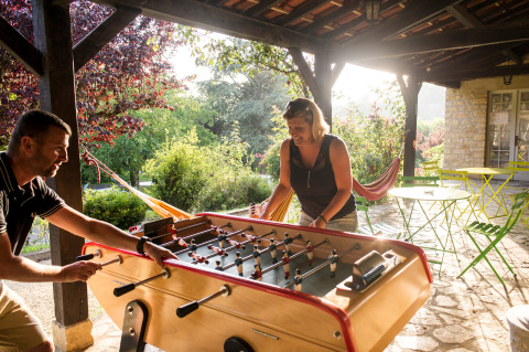 Dos personas juegan al futbolín en una terraza cubierta en Huttopia Sarlat, un parque de vacaciones en Francia.