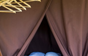 Interieur van een safaritent met tweepersoonsbed, hangers en bruine gordijnen bij Huttopia Calvados - Normandie.