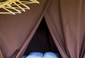 Binnenkant van safaritent met dubbel bed, kleerhangers en bruine gordijnen bij Huttopia Calvados - Normandie.