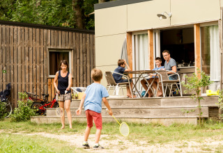 Familie nyder udendørsaktiviteter ved en mobilhytte i Huttopia Sarlat, Frankrig, med børn der leger badminton.