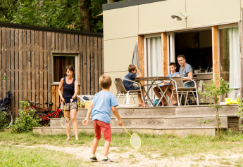 Familie nyder udendørsaktiviteter ved en mobilhytte i Huttopia Sarlat, Frankrig, med børn der leger badminton.