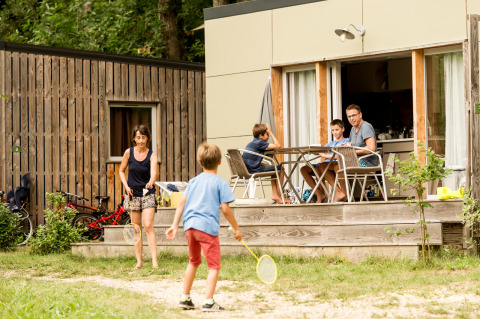 Familie spielt Badminton und entspannt auf der Terrasse eines Mobilheims in Huttopia Sarlat, Frankreich.