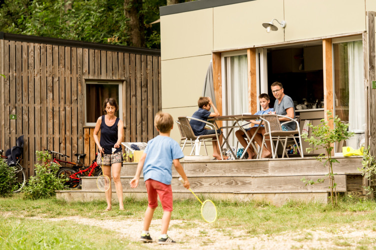 Family enjoys outdoor time at the Mobile home Vancouver, Huttopia Sarlat, France, with kids playing badminton.