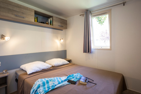 Dormitorio en Mobile home Vancouver en Huttopia Sarlat, Francia, con cama doble y ventana luminosa.