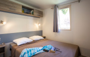 Dormitorio en Mobile home Vancouver en Huttopia Sarlat, Francia, con cama doble y ventana luminosa.