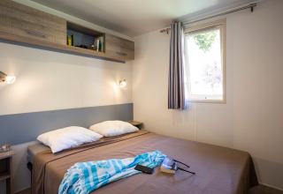 Dormitorio en Mobile home Vancouver en Huttopia Sarlat, Francia, con cama doble y ventana luminosa.