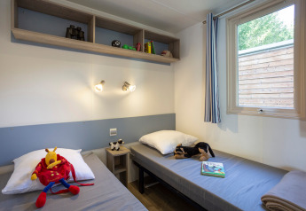 Due letti singoli con giocattoli e libri in una cameretta al Mobile home Vancouver, Huttopia Sarlat, Francia.