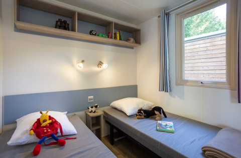 Due letti singoli con giocattoli e libri in una cameretta al Mobile home Vancouver, Huttopia Sarlat, Francia.