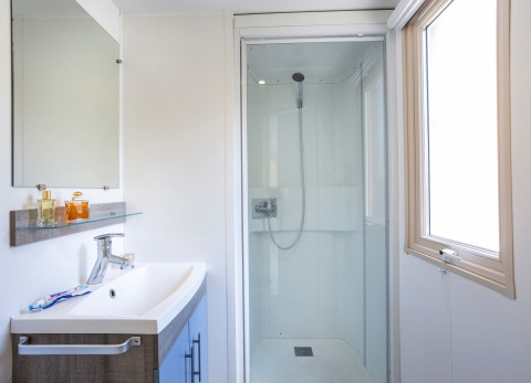 Salle de bain lumineuse et moderne au Mobile home Vancouver avec douche, lavabo, miroir et fenêtre.