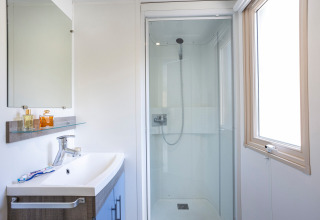 Salle de bain lumineuse et moderne au Mobile home Vancouver avec douche, lavabo, miroir et fenêtre.