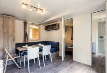 Lichte, moderne woonkamer van een stacaravan met eethoek en toegang tot slaapkamer en badkamer bij Huttopia Sarlat.