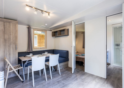 Salon moderne et lumineux d’un mobil-home avec coin repas, vue sur chambre et salle de bain à Huttopia Sarlat.