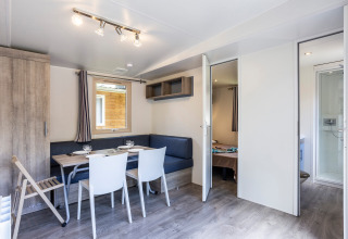 Bright, modern mobile home living area with dining setup and access to bedroom and bathroom at Huttopia Sarlat.