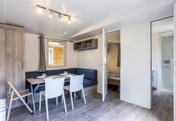 Zona giorno luminosa e moderna in casa mobile con tavolo da pranzo e accesso a camera e bagno a Huttopia Sarlat.