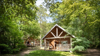 Cabaña de madera en el bosque de Huttopia Rambouillet, Francia, rodeada de naturaleza exuberante.