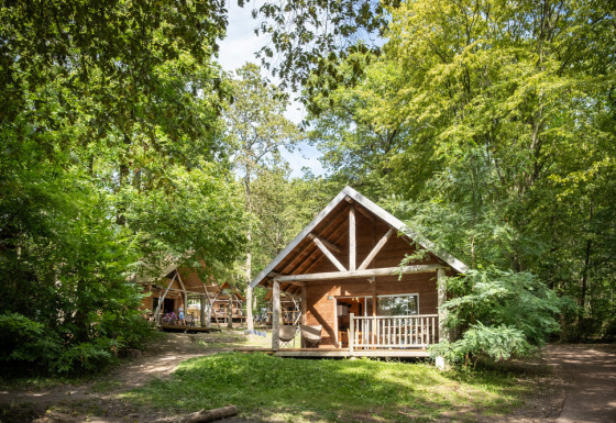 Houten hut te midden van het groen bij Huttopia Rambouillet in Frankrijk, rust en natuurpracht.