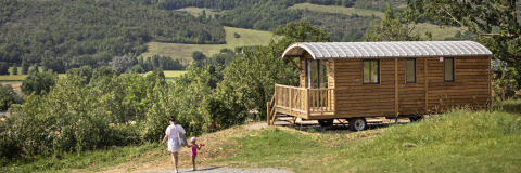 Jolie roulotte en bois à Huttopia Rambouillet, France, entourée de verdure et de collines verdoyantes.
