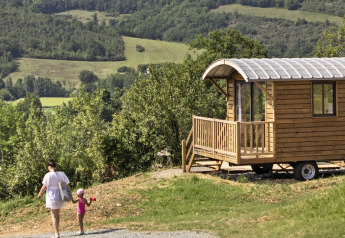 Holzige Zigeunerwagenhütte bei Huttopia Rambouillet in Frankreich mit grüner Hügellandschaft und Spaziergängern.