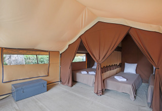 Intérieur d'une tente safari avec deux lits simples, serviettes propres, coffre et vue sur la nature.