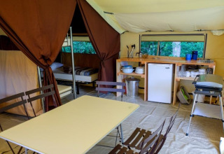 Interior de una tienda safari Toile&bois Classic en Huttopia Sarlat, Francia, con mesas, camas y cocina.