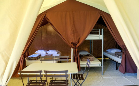 Vista interna di una tenda safari Toile&bois Classic a Huttopia Sarlat, Francia, con letti e tavolo.