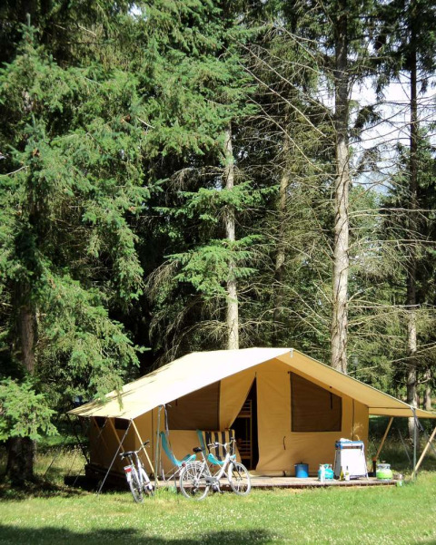Tienda safari Toile&bois Classic en Huttopia Sarlat, Francia, rodeada de bosque y equipo de acampada.