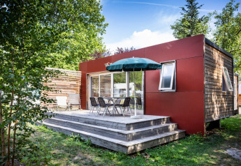 Casa mobile Vancouver a Huttopia Sarlat, Francia, con terrazza in legno, tavolo, sedie e ombrellone verde.