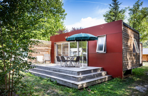 Casa mobile Vancouver a Huttopia Sarlat, Francia, con terrazza in legno, tavolo, sedie e ombrellone verde.