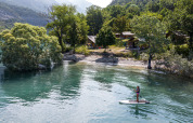 En person står på paddleboard på en sø omgivet af træer og feriehytter i Provence-Alpes-Côte d’Azur.