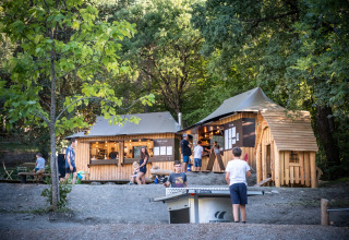 Gezinnen ontspannen en kinderen spelen tafeltennis aan een houten hut in Huttopia Lac de Serre Ponçon, Frankrijk.