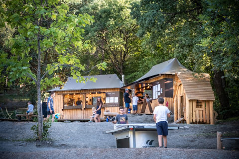 Gezinnen ontspannen en kinderen spelen tafeltennis aan een houten hut in Huttopia Lac de Serre Ponçon, Frankrijk.