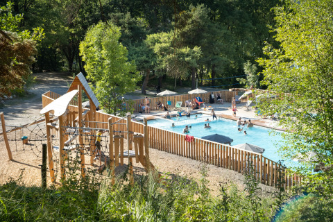Piscina al aire libre y zona de juegos infantiles en Huttopia Lac de Serre Ponçon, rodeada de árboles en Francia.