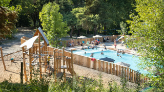 Piscina al aire libre y zona de juegos infantiles en Huttopia Lac de Serre Ponçon, rodeada de árboles en Francia.