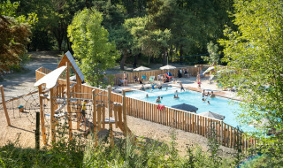 Piscina al aire libre y zona de juegos infantiles en Huttopia Lac de Serre Ponçon, rodeada de árboles en Francia.