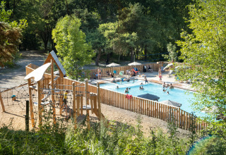 Piscina al aire libre y zona de juegos infantiles en Huttopia Lac de Serre Ponçon, rodeada de árboles en Francia.
