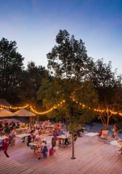 Reunión nocturna en Huttopia Lac de Serre Ponçon con luces de guirnalda y familias cenando al aire libre.