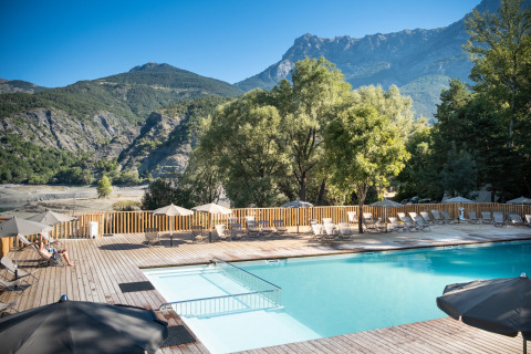 Piscina exterior con tumbonas y sombrillas, rodeada de montañas en Huttopia Lac de Serre Ponçon, Francia.