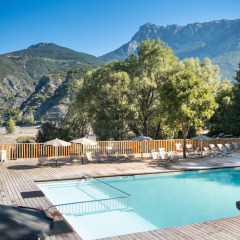 Piscina exterior con tumbonas y sombrillas, rodeada de montañas en Huttopia Lac de Serre Ponçon, Francia.