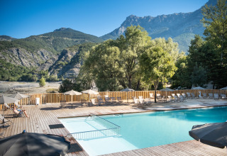 Piscina all'aperto con lettini e ombrelloni, circondata da montagne a Huttopia Lac de Serre Ponçon, Francia.