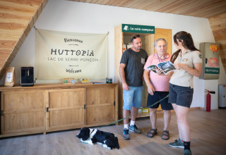 Receptioniste helpt twee mannen met hond bij Huttopia Lac de Serre Ponçon, Provence-Alpes-Côte d’Azur, Frankrijk.