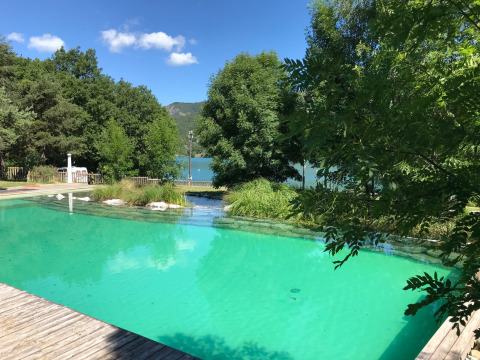 Piscina natural rodeada de árboles y vista al lago en Huttopia Lac de Serre Ponçon, parque turístico en Francia.