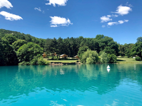 Lago turquesa reflejando árboles y tiendas en Huttopia Lac de Serre Ponçon, parque vacacional en el sureste de Francia.