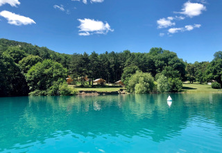 Lago turquesa reflejando árboles y tiendas en Huttopia Lac de Serre Ponçon, parque vacacional en el sureste de Francia.