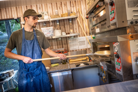 Un hombre con delantal prepara pizza en la cocina de Huttopia Lac de Serre Ponçon, Francia.
