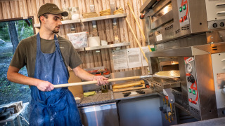 Un hombre con delantal prepara pizza en la cocina de Huttopia Lac de Serre Ponçon, Francia.