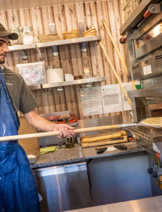 Un hombre con delantal prepara pizza en la cocina de Huttopia Lac de Serre Ponçon, Francia.