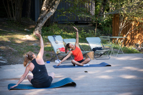 Dos mujeres hacen yoga al aire libre sobre esterillas en Huttopia Lac de Serre Ponçon, Francia.